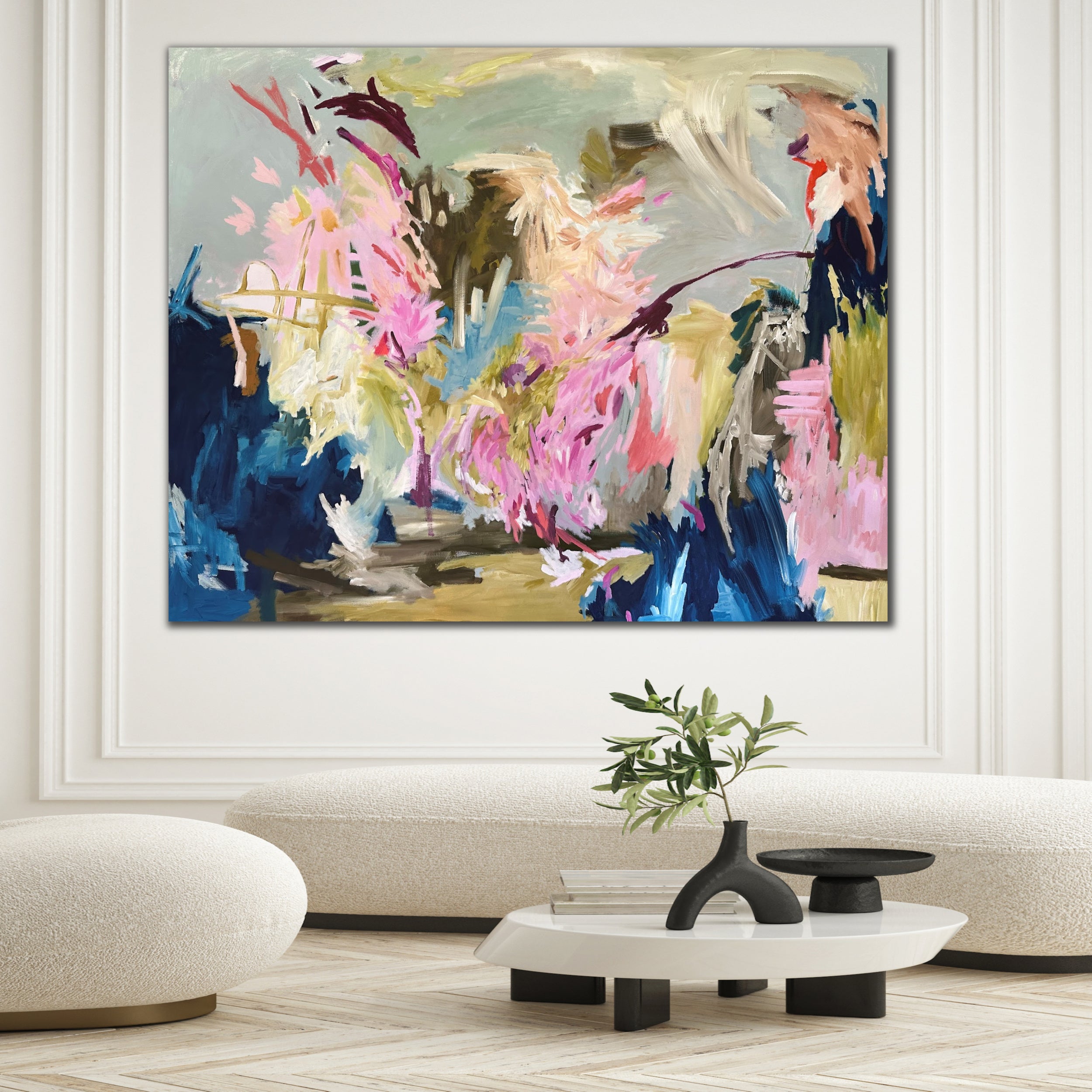 A large abstract painting with vibrant pink, blue, olive green, and citron brushstrokes, displayed on a white wall in a contemporary living room.