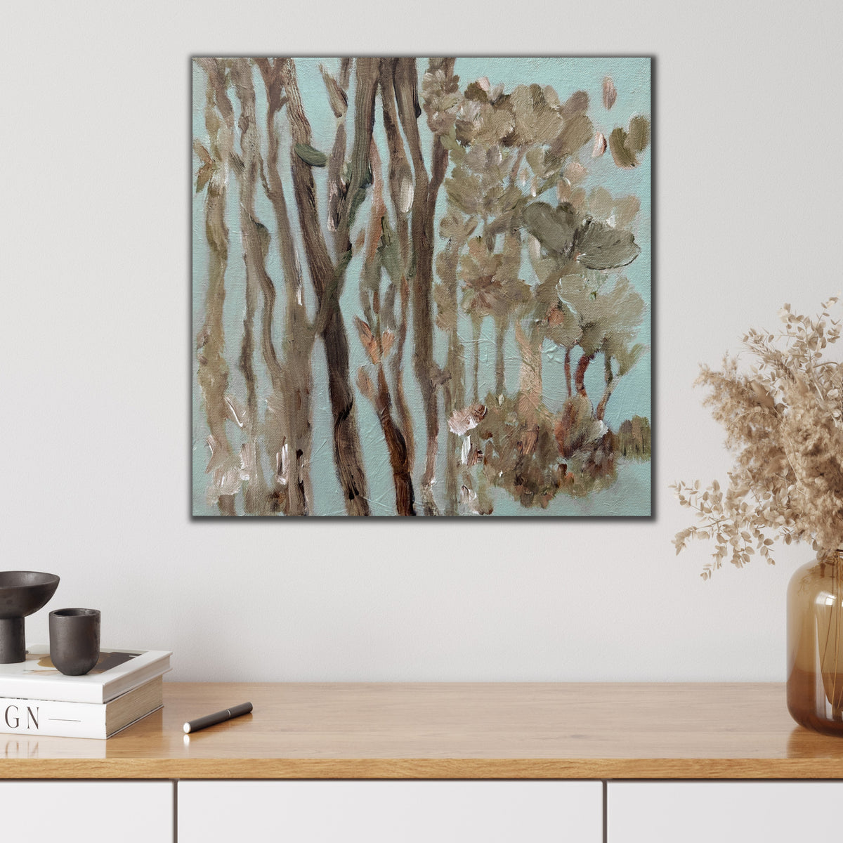 A small square painting of Australian gum trees hanging on wall in modern home with neutral furnishings. 