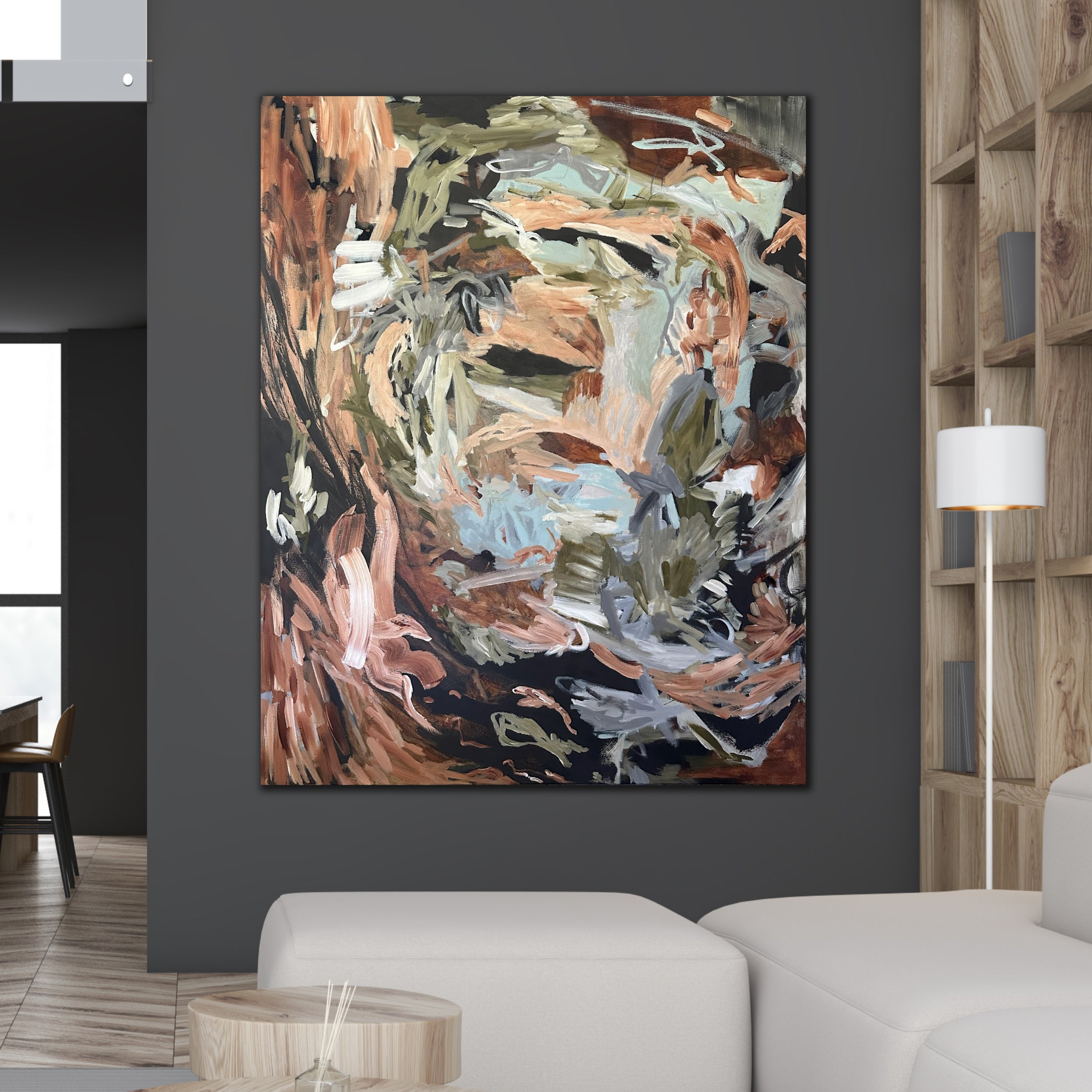 A large abstract artwork with expressive brushstrokes in brown, beige, black, white, and muted blue, displayed on a dark grey wall in a modern living room setting.