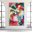 A large abstract canvas painting with vibrant splashes of pink, red, orange, green, blue, black, and white, displayed on a neutral coloured wall between two tall arched windows.