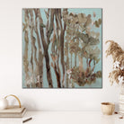 Square painting of nature tree scape with soft blue background and tree trunks and foliage in natural colours of greens and browns hanging on white wall in modern interior. 