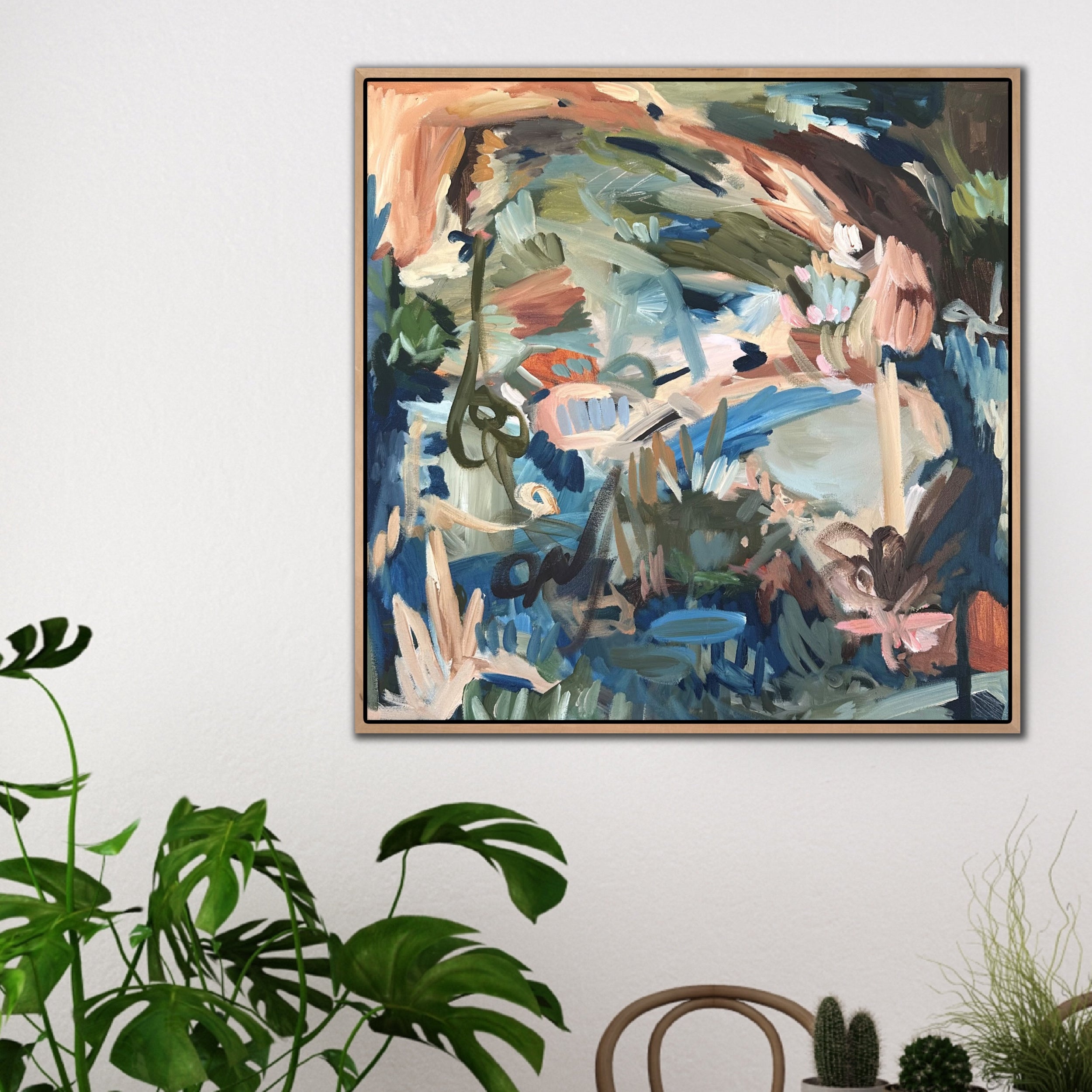Square abstract painting of natural landscape hanging on wall in dining room of modern home interior filled with plants