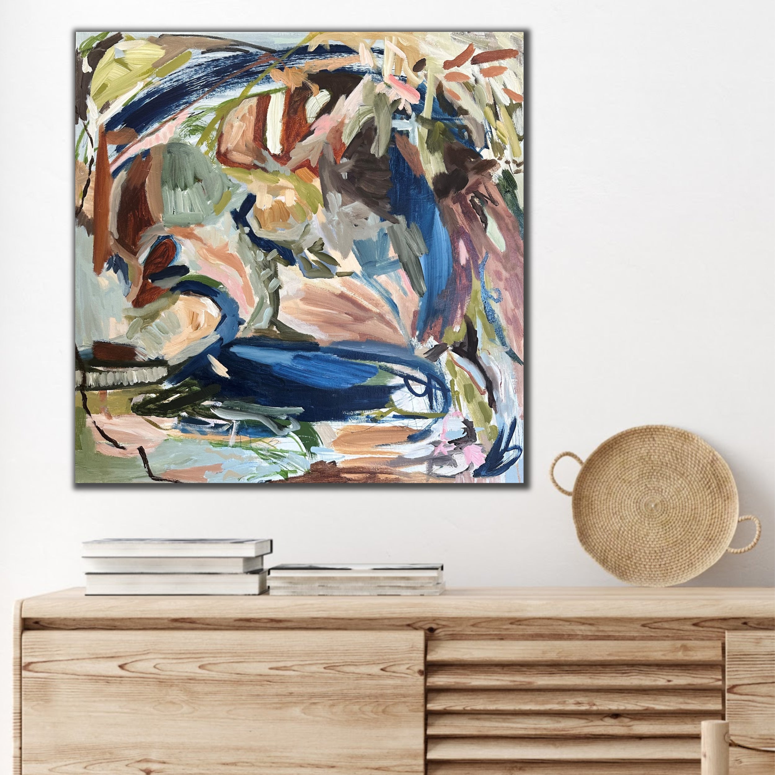 Square abstract expressionist artwork in blue, green, brown and beige hanging on wall in modern interior with natural furnishings
