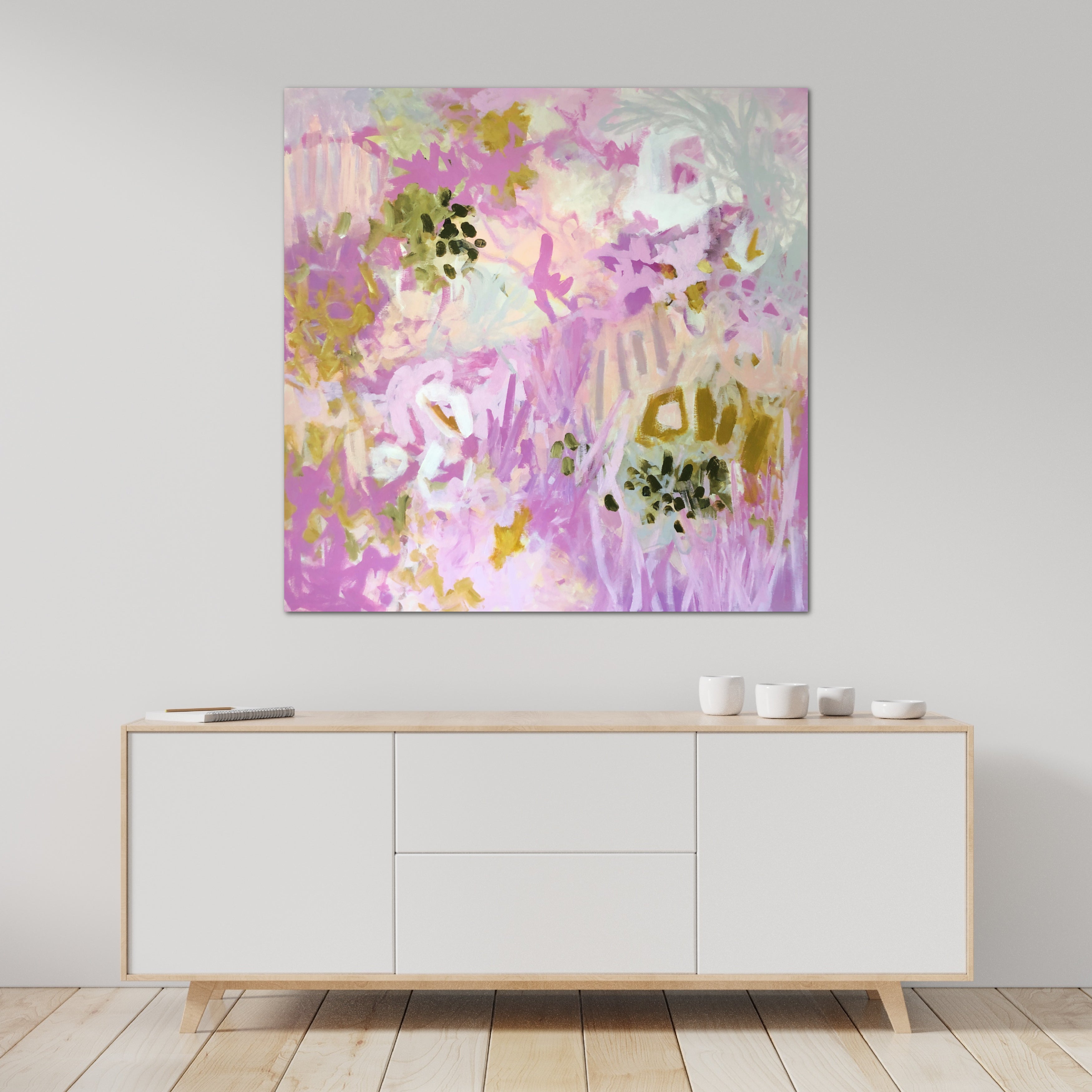 Square, abstract landscape painting with pretty botanical elements hanging on wall in room with neutral, contemporary decor